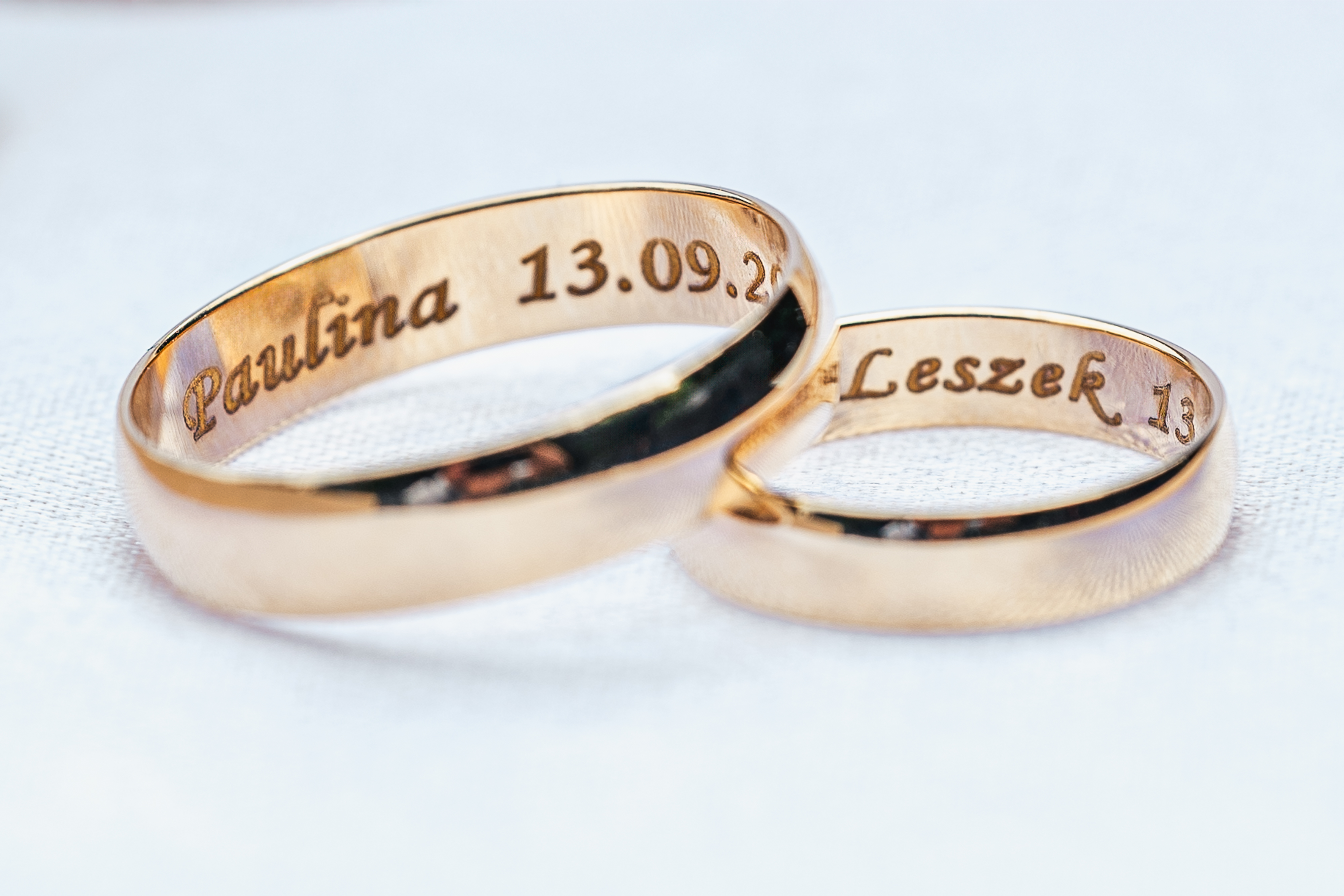 Złote obrączki ślubne z wygrawerowanymi imionami i datą ślubu.