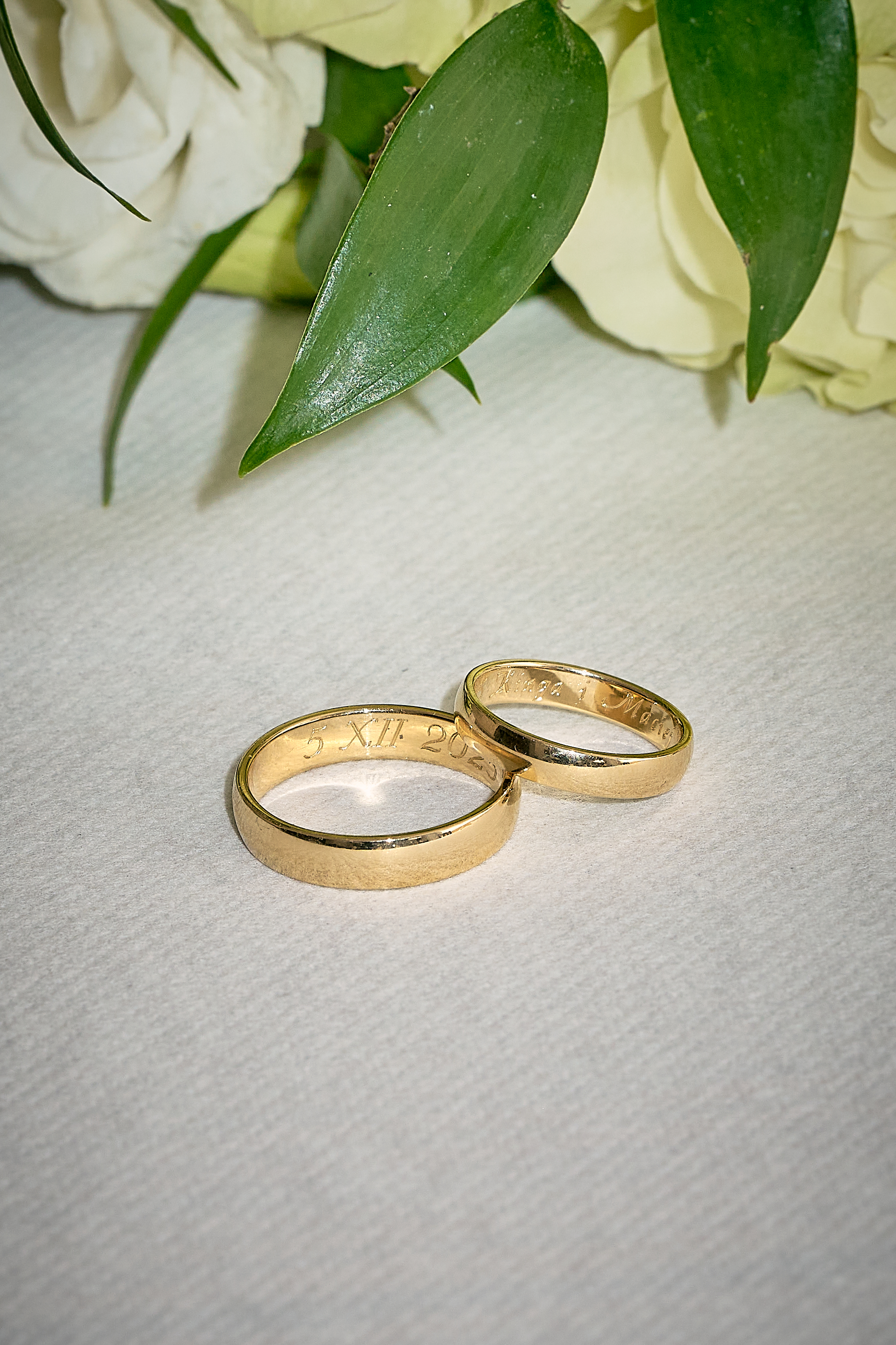 Złote obrączki ślubne ułożone na stole w otoczeniu dekoracji kwiatowych.