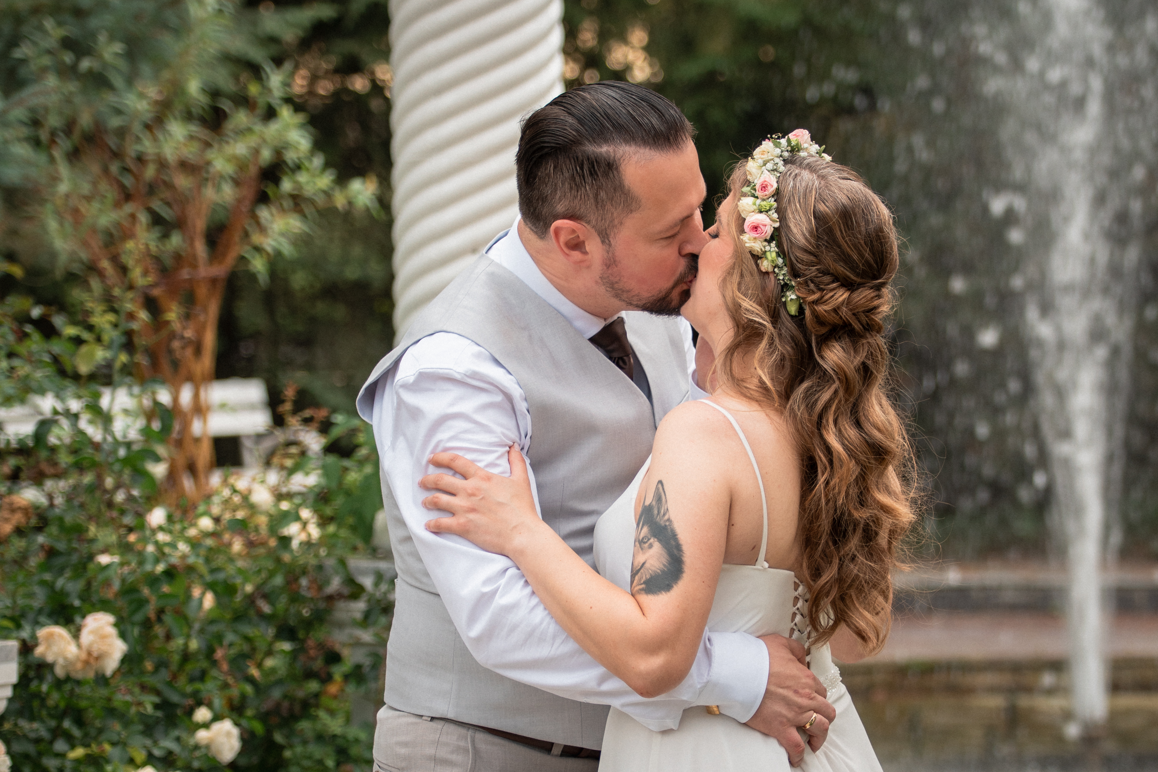 Romantyczny pocałunek pary młodej przy fontannie w ogrodzie.